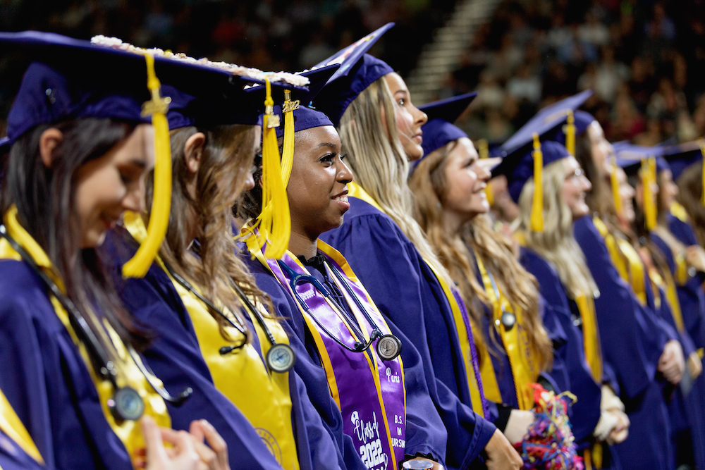 Graduates stand to be recognized at commencement ceremonies
