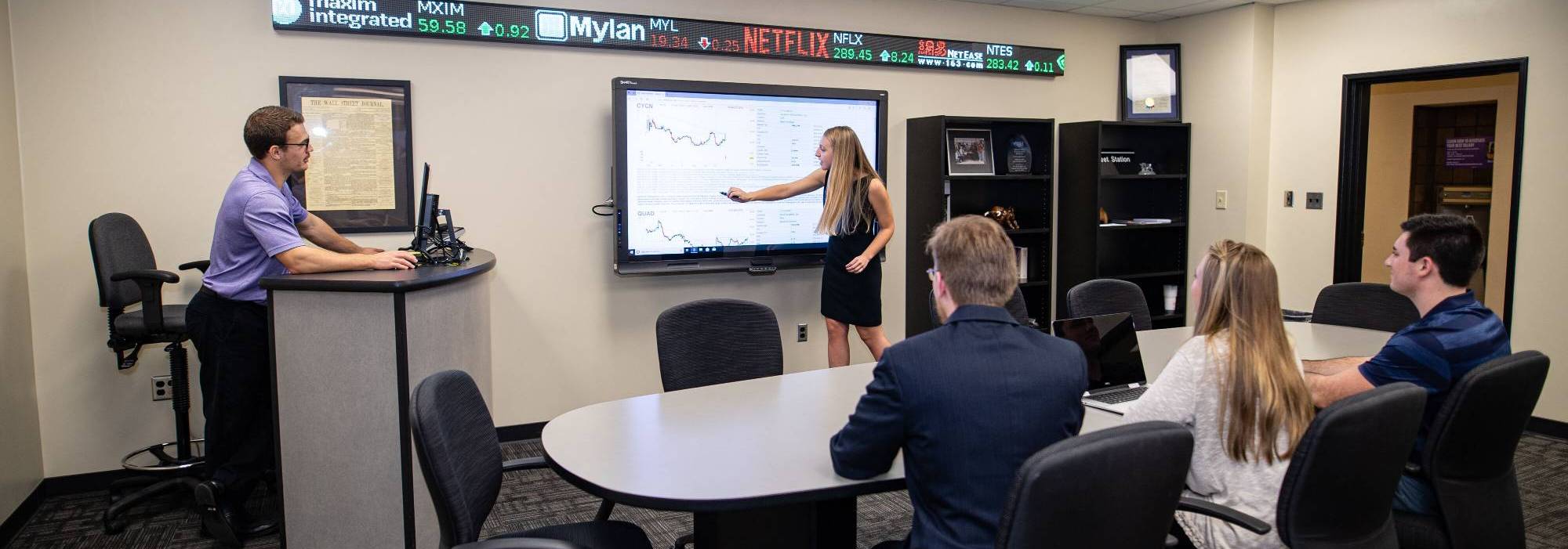 students giving a presentation with a large interactive screen and a podium