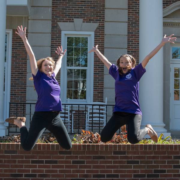 Two students in purple shirts leaping into the air.