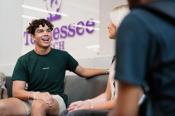 Students chat in a campus lounge, with one laughing on a couch beneath a Tennessee Tech wall sign.