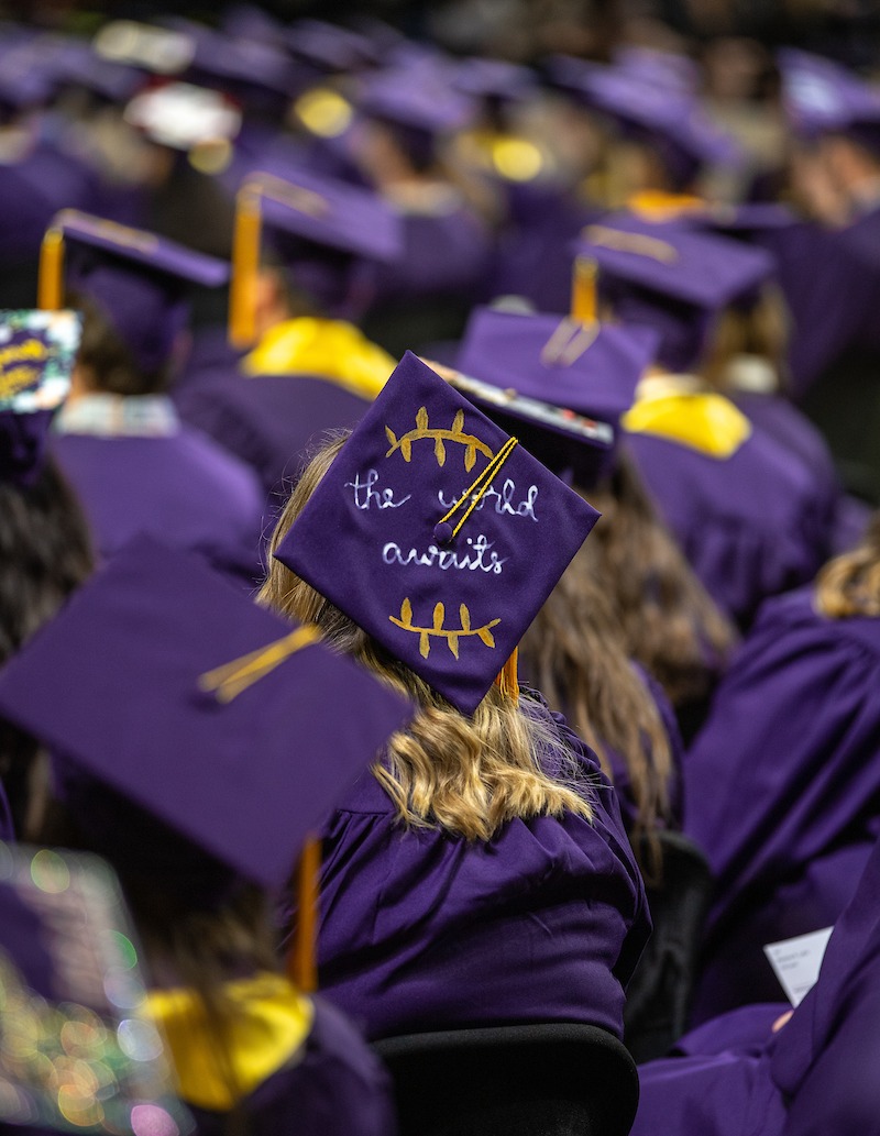Graduating student wearing a cap that says 'The World Awaits'