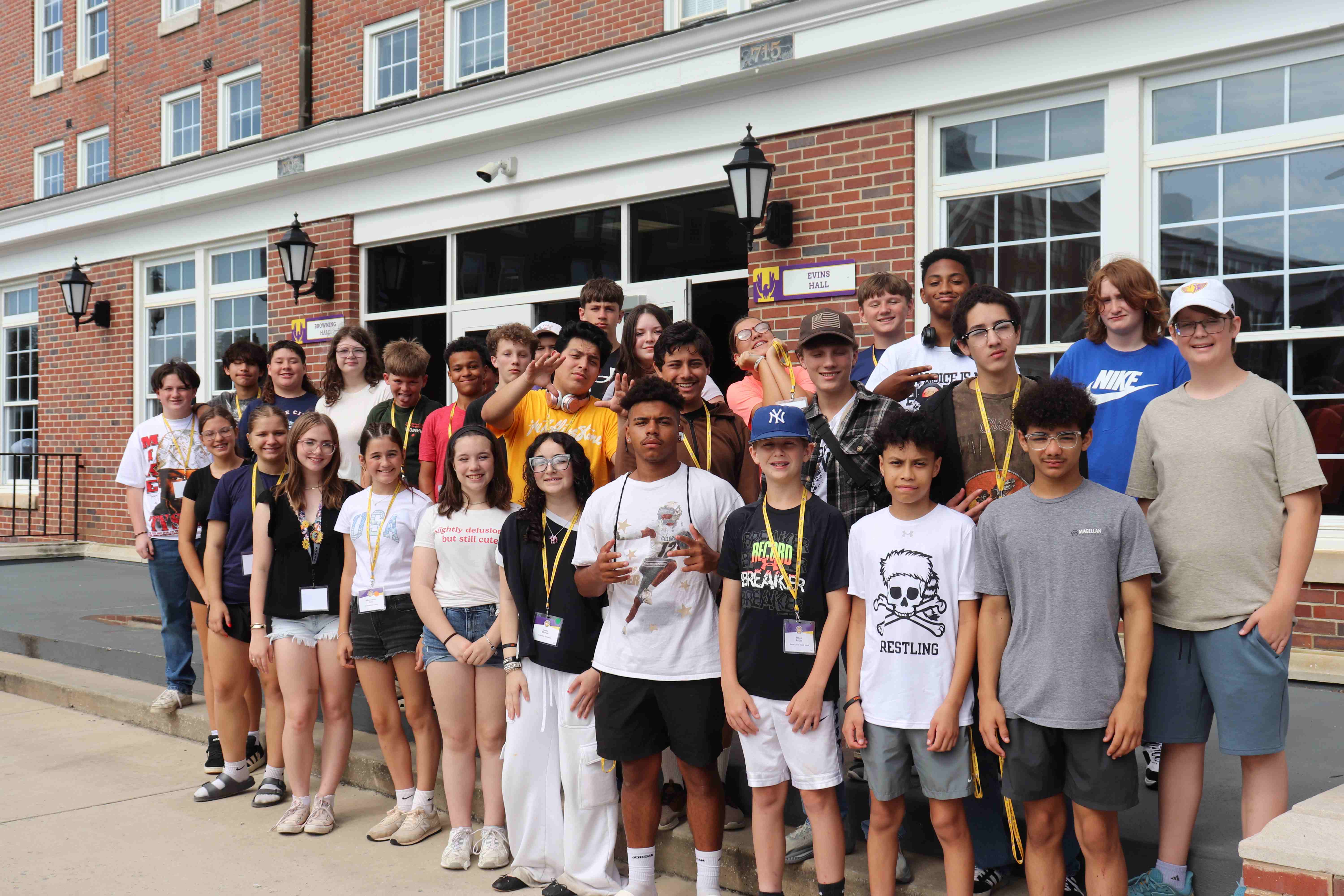 A large, diverse group of students wearing name tags and lanyards pose together outside the brick entryway of Evins Hall.