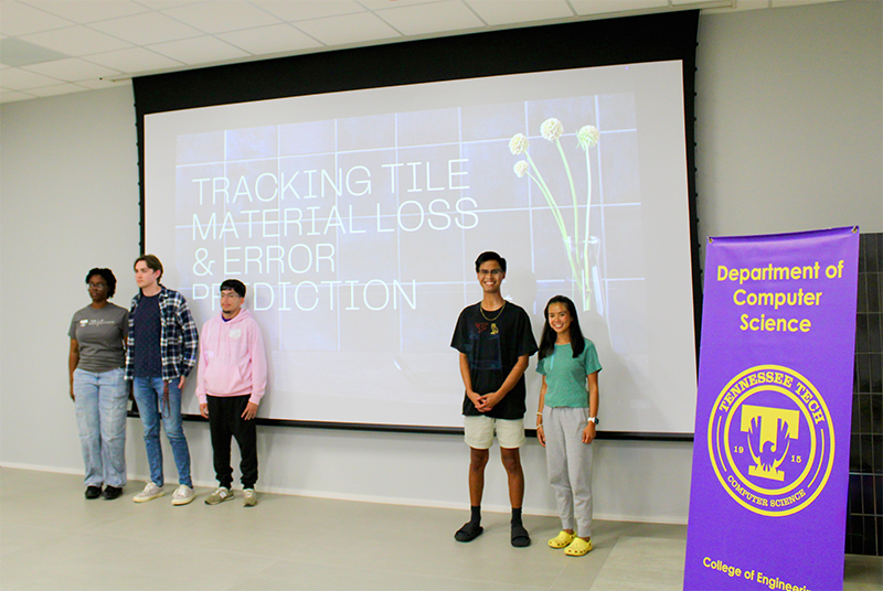 Five hackathon-winning students stand together in front of screen