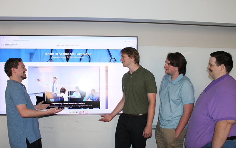 Four people smile and pose in front of screen displaying their nonprofit work.