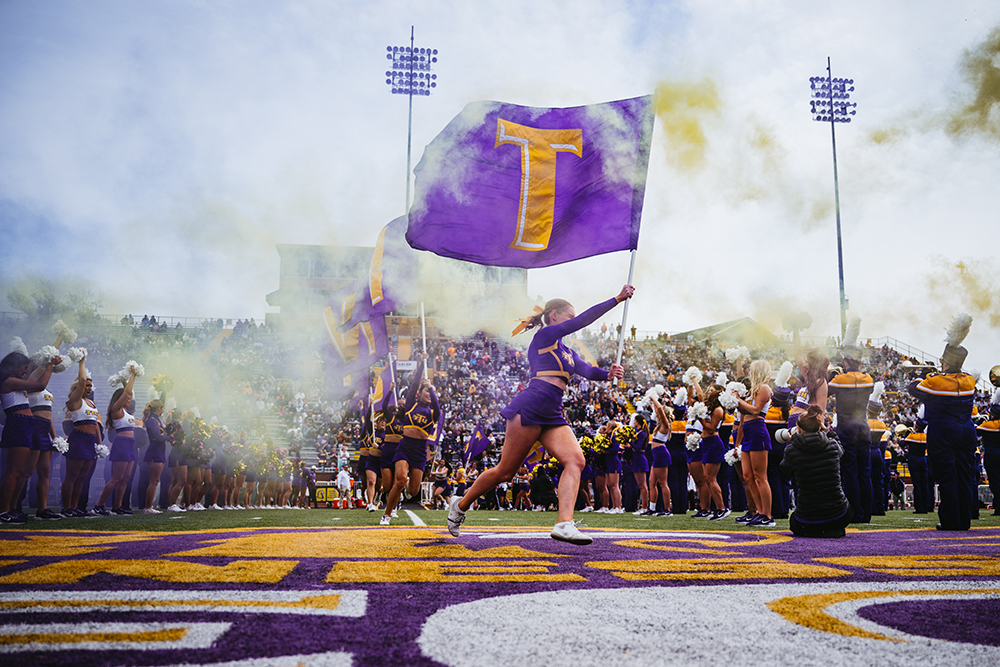homecoming photo of cheerleader on the football field running with a Tech flag.