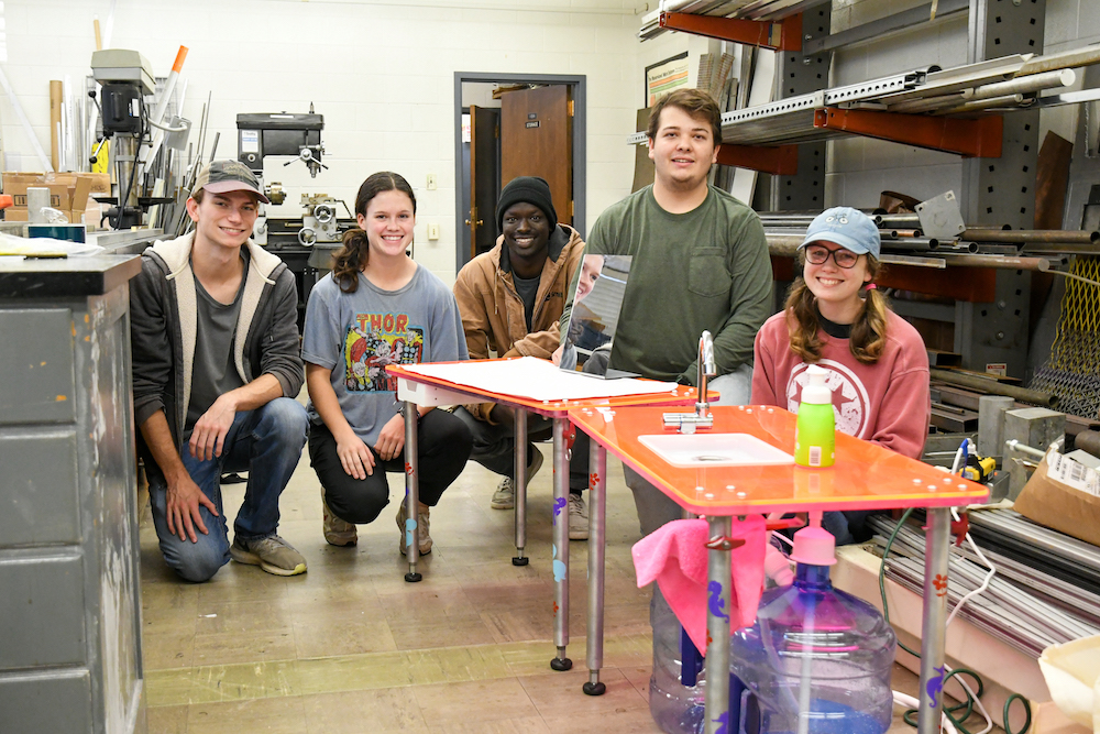 Students Wyatt Been, Meredith Nye, Obang Lwangmianga, Luke Miller and Jessie Gray stand with the table they designed for a young girl in a wheel chair.