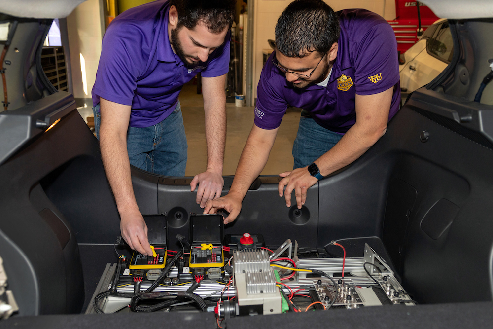 Two graduate students work on the electric components of a vehicle.