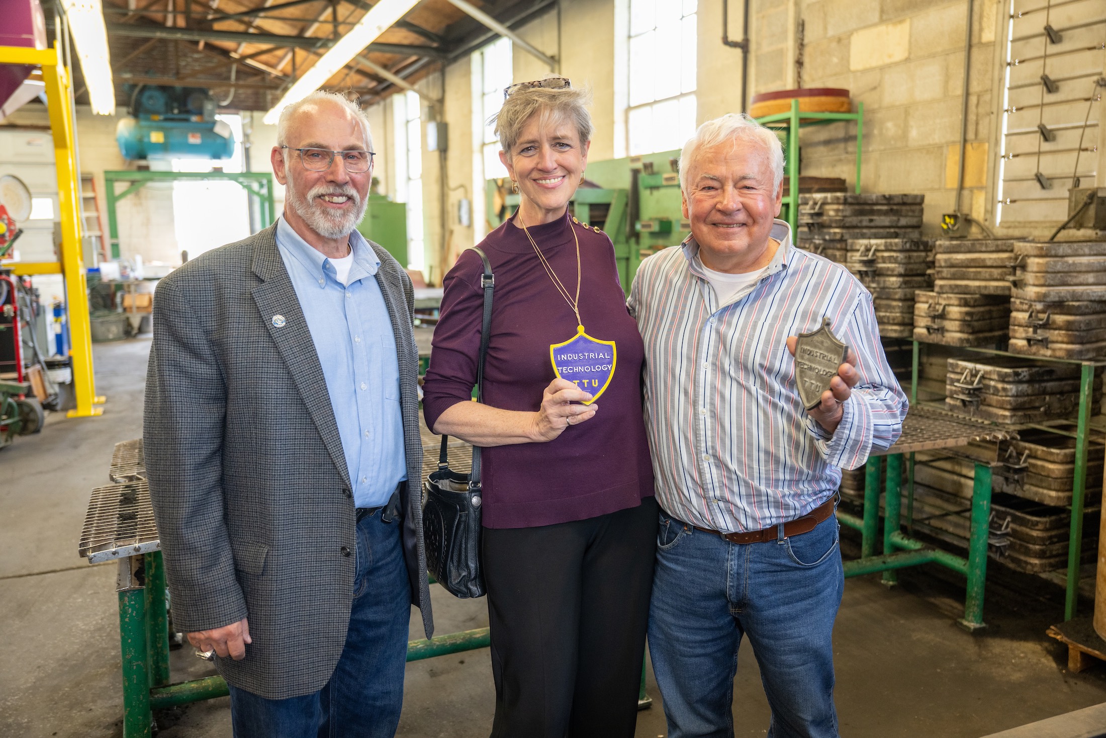 From left: Fred Vondra, chair of the Department of Manufacturing and Engineering Technology, Trudy Harper, chair of the Board of Trustees, and Gary Durham, former Tech student, are pictured inside the current Tech foundry. Harper is holding a metal placard Durham made at the foundry during his years as a Tech student and later gifted to her. Durham is holding the original mold used to make the placard. 