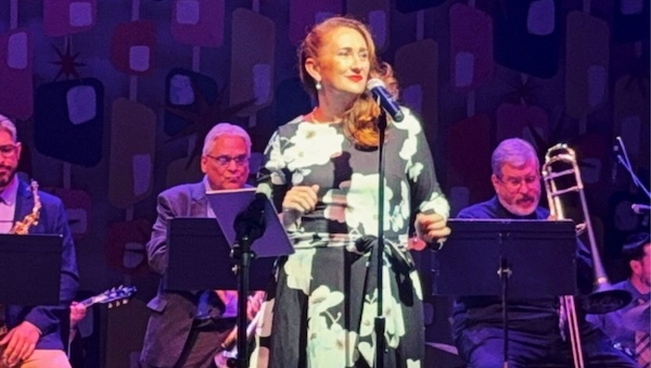 Mellisa Ellis is seen performing on a stage with musicians in the background