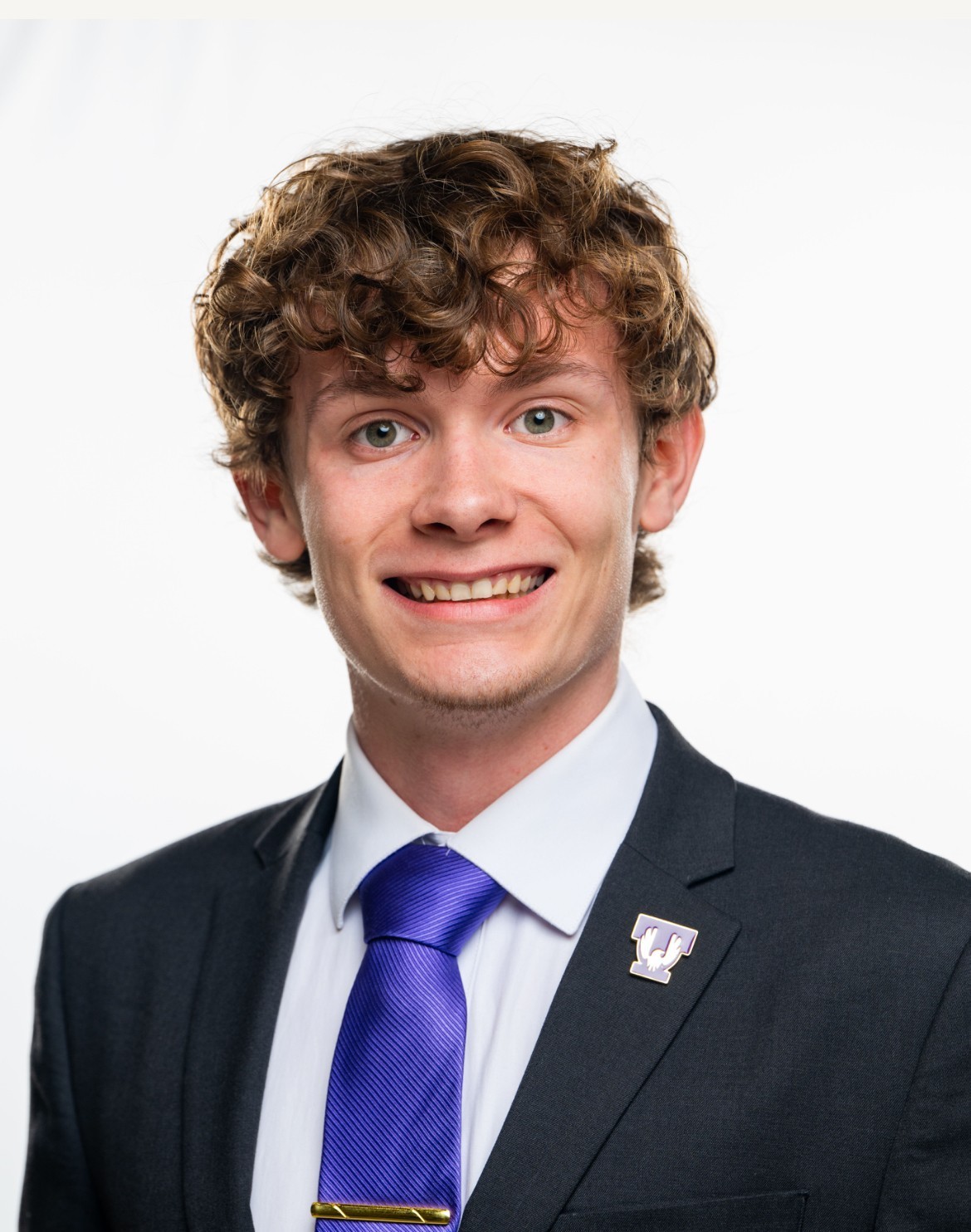 Headshot of Harrison Simpson smiling in a dark suit and purple tie. 