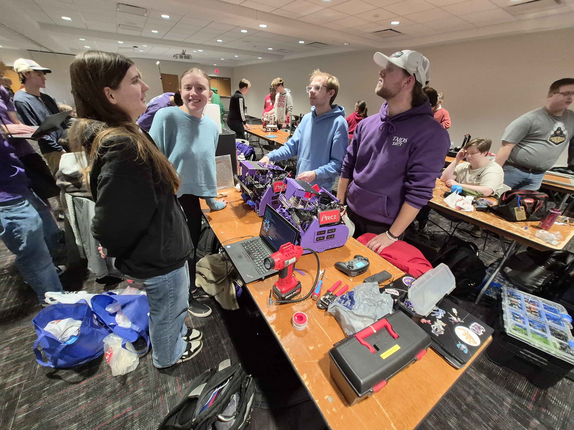 Action shot of students gathered around a table making adjustments to a robot.