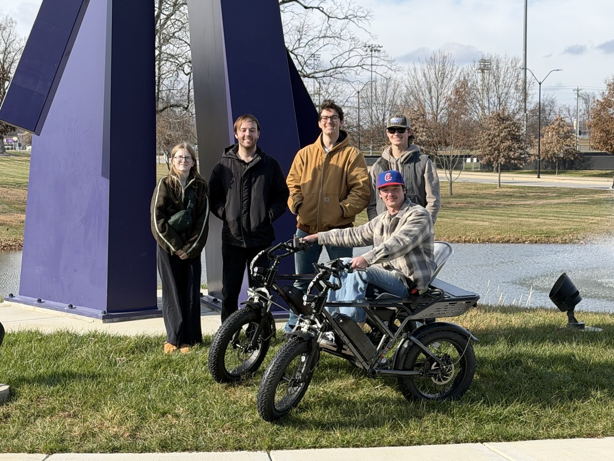 A student in an all-terrain wheelchair smiles as others stand behind him. 