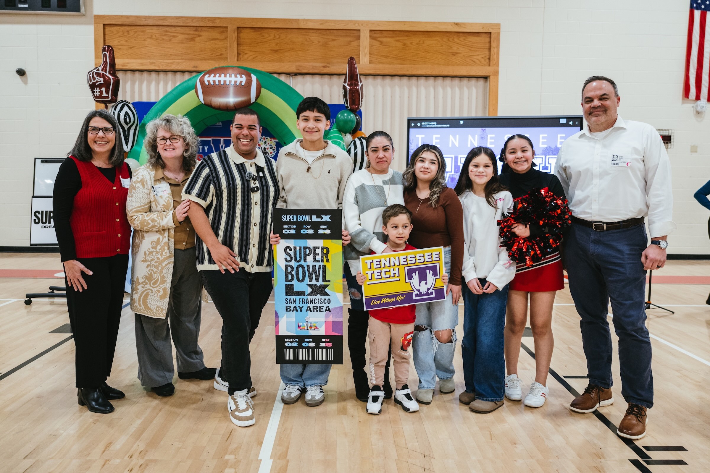 A smiling Eduardo Mendez is pictured in a group photo holding a Super Bowl LX sign.