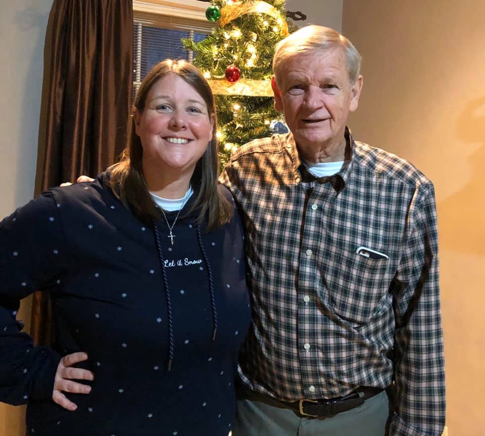 Jennifer Winningham and her dad smile in front of a Christmas tree at their family home. 