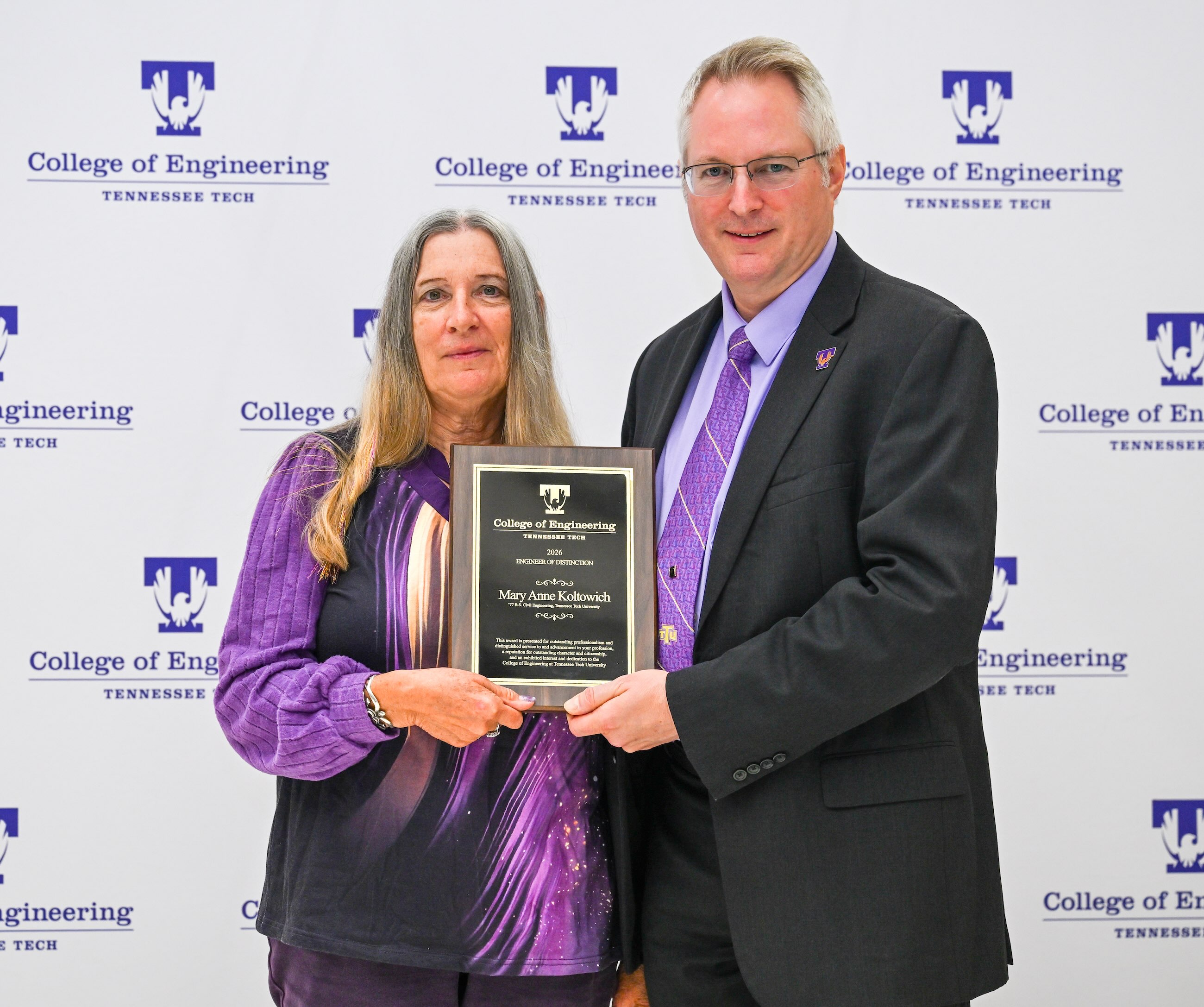 Mary Anne Koltowich and Dean Joseph Slater stand and hold an award placard.