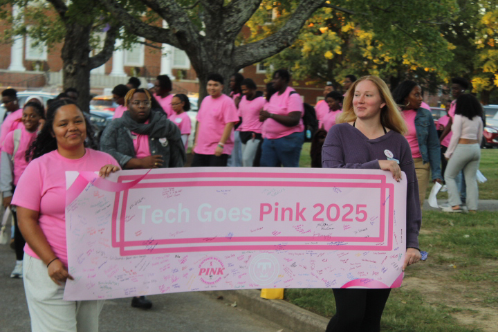 Two students look ahead carrying a large pink banner while others file in behind them. 
