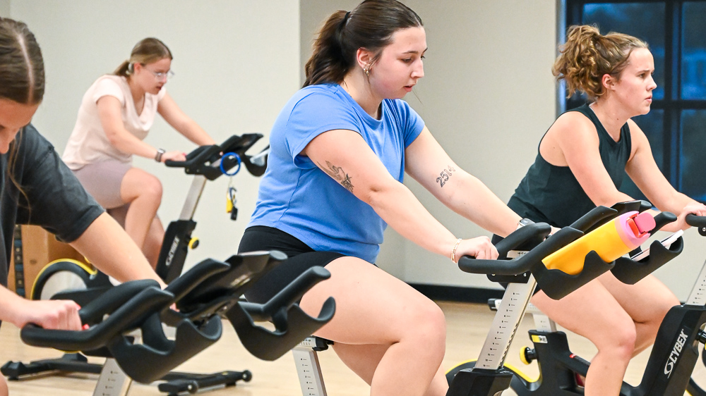 Group of students cycling indoors during a group fitness class.