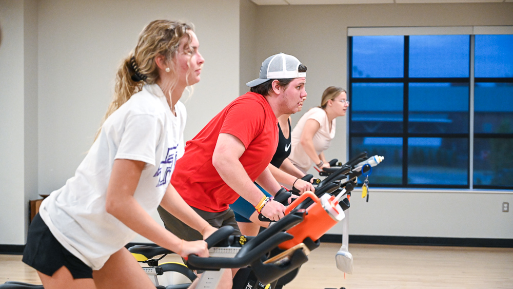 Students cycling indoors during a group fitness class.