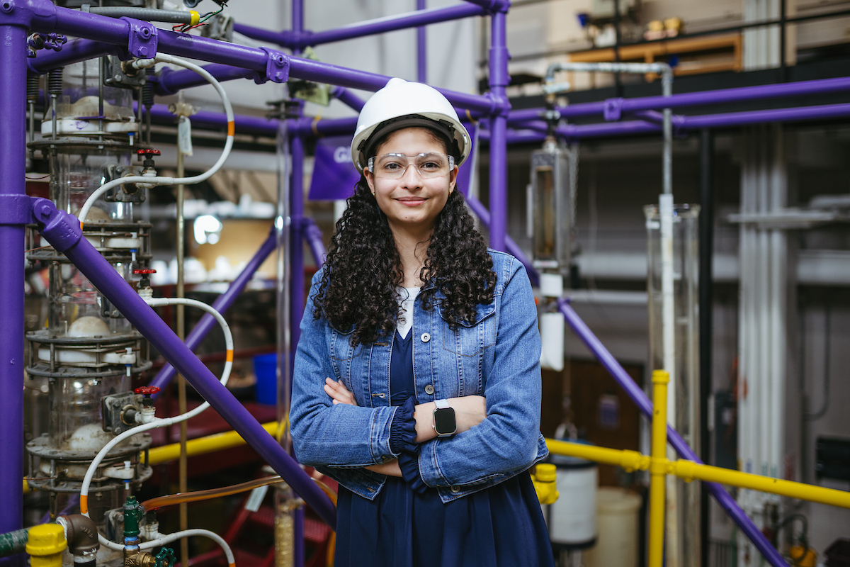 Yulieth Mercado stands in front of purple and gold pipes in a chemical engineering lab.