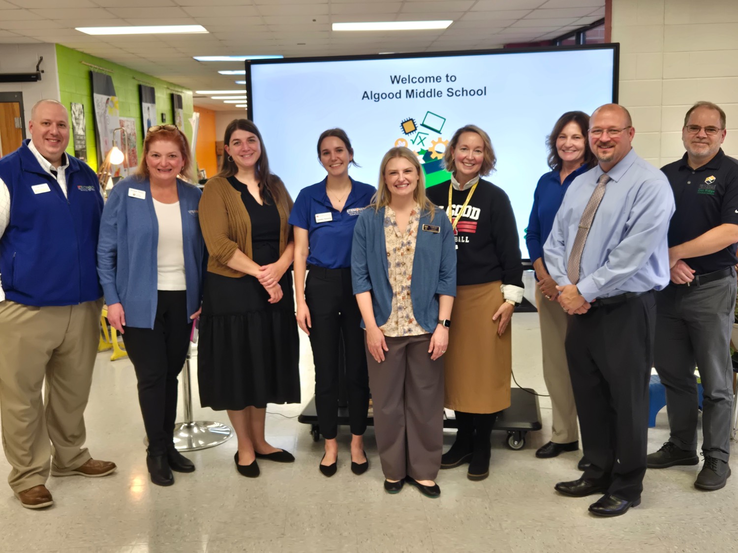 group of people smiling. there is a screen behind them that reads "Welcome to Algood Middle School"
