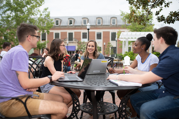 A group of students sit around a table on the plaza with laptops.