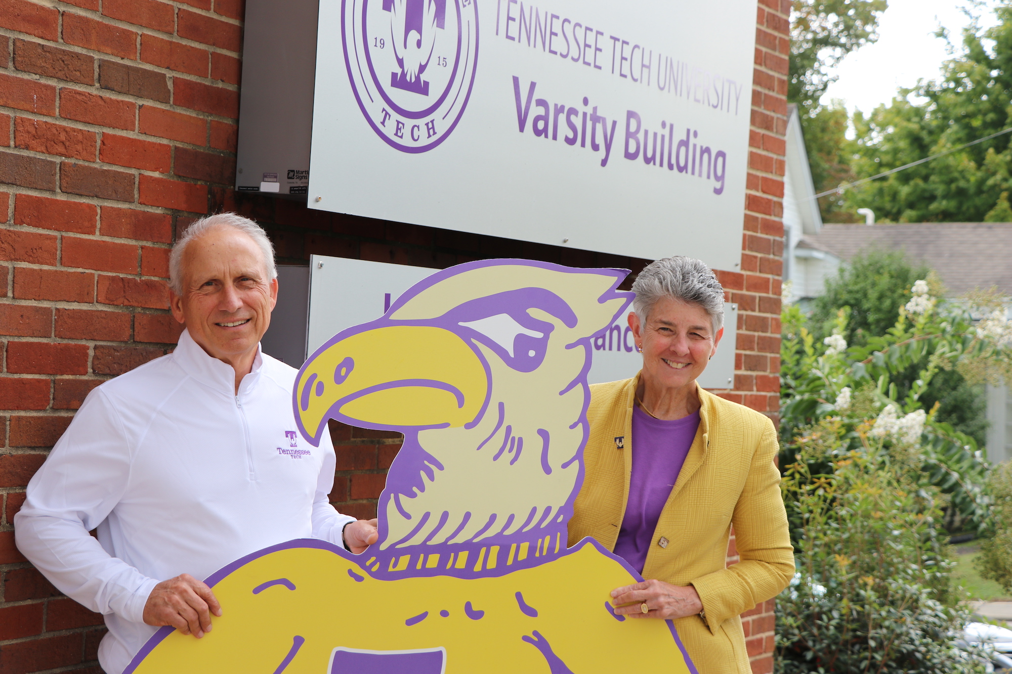 A photo of Ottis Phillips and Dianne Murphy in front of the Varsity Building. They are smiling and standing behind a cardboard cutout of Tommy Tech.