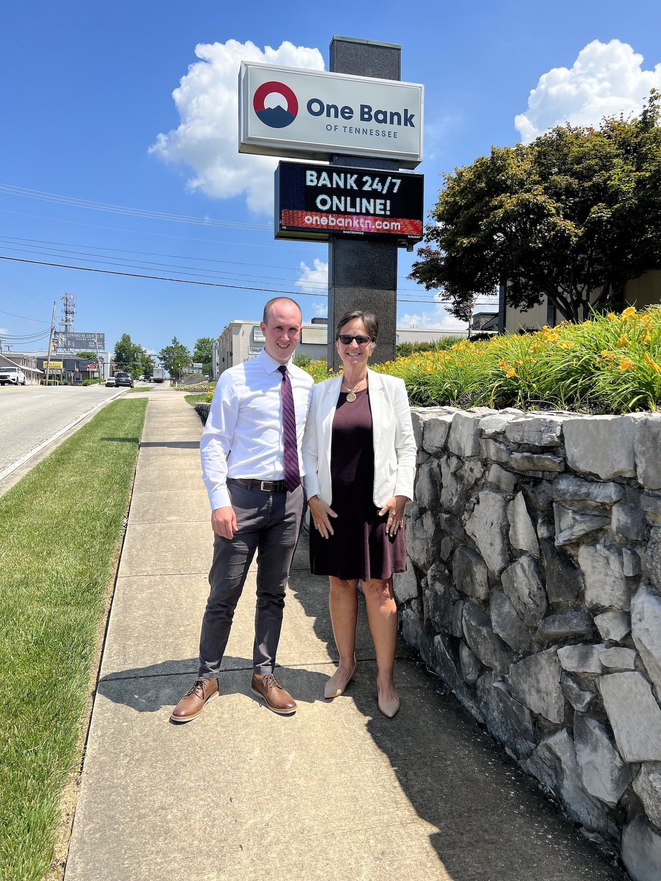 a man and woman stand in front of the sign for One Bank