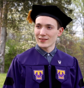 A male student standing outside in graduation regalia.