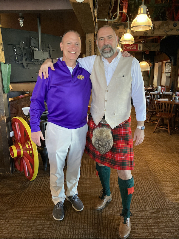 Charles White stands wearing a kilt with his arm around Development Director Bobby Taylor