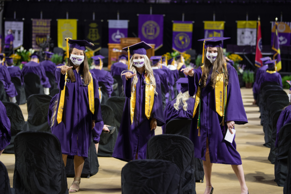  A photo of three students in graduation robes and masks giving "wings up."