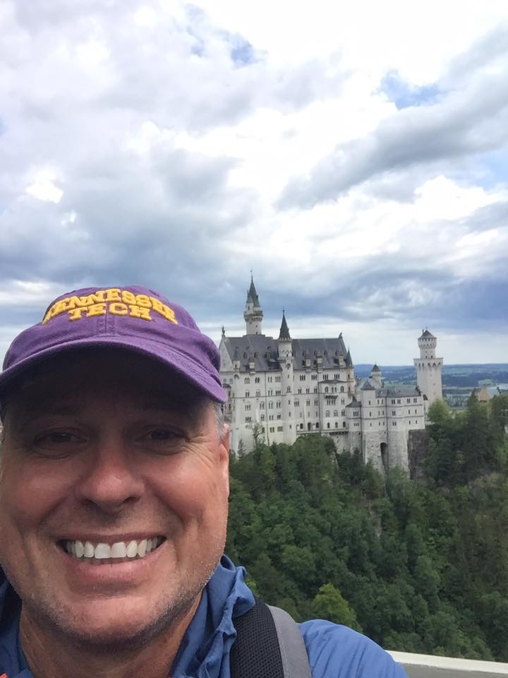 Mike Duke smiles in front of a castle in Germany with his Tennessee Tech hat.