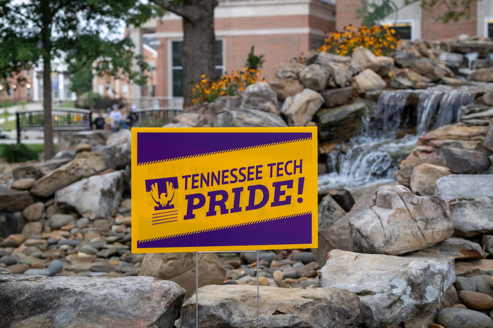 A photo of a purple and gold Tennessee Tech Pride sign in front of the stone fountain in Centennial Plaza.