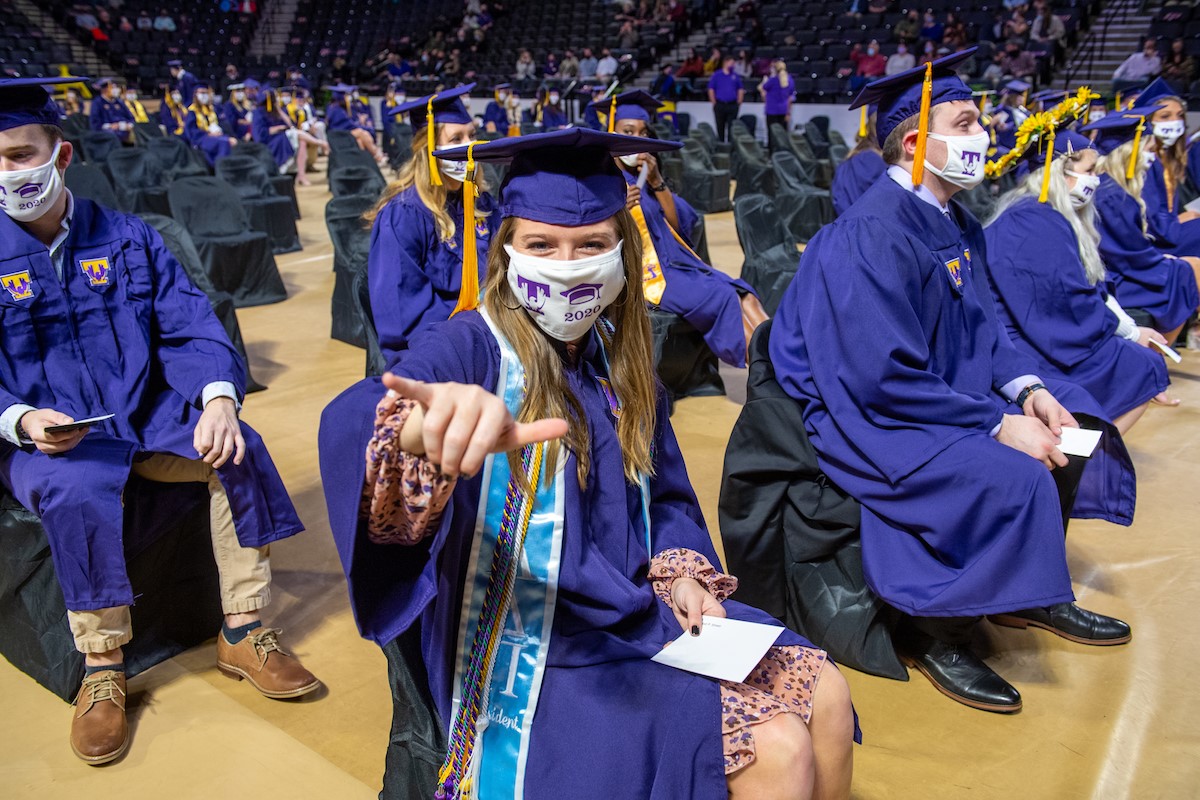 A photo of socially distanced students during commencement. One of the students is giving the camera the "wings up" sign.