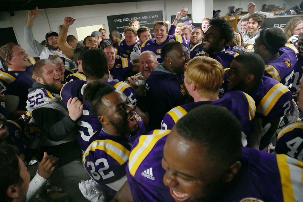The football team celebrates in the locker room with Coach Alexander.