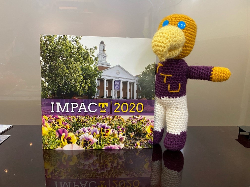 a little crocheted Awesome Eagle doll with a copy of the 2020 Impact