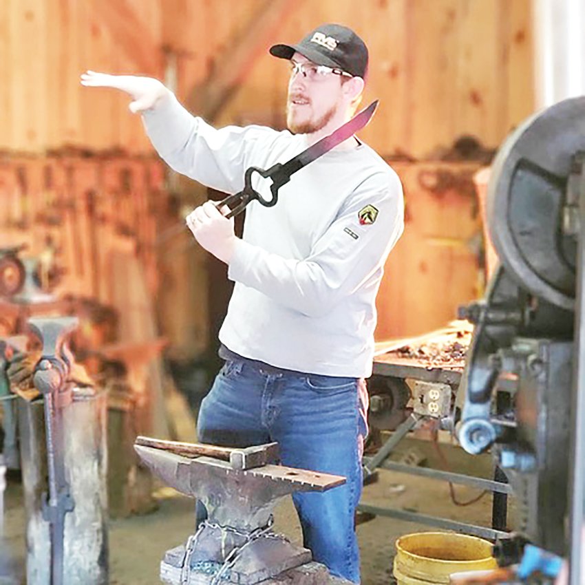 Joshua Foran holding a glowing forged sword in a blacksmith shop