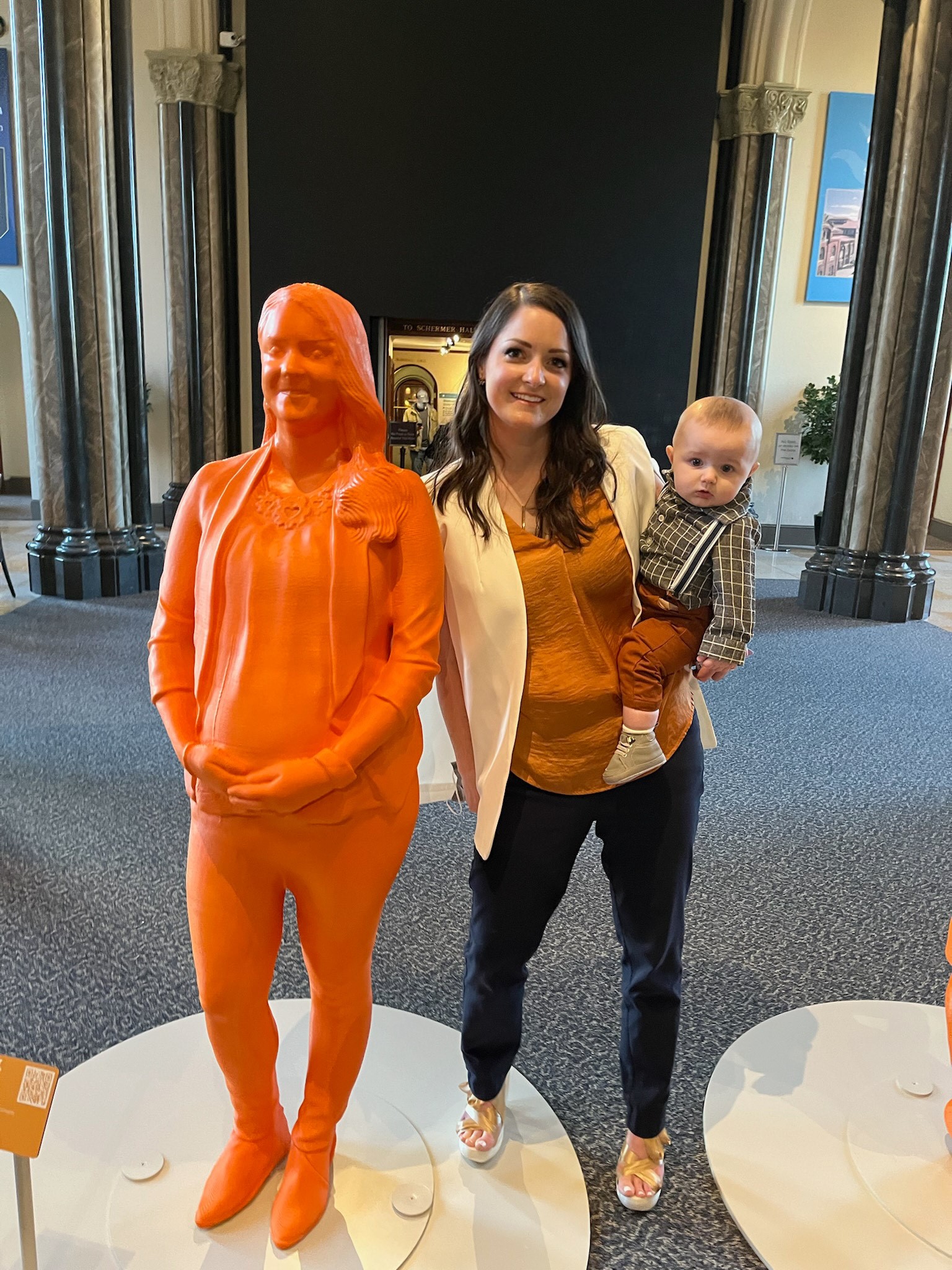Amy Elliott holding her baby next to an orange 3D printed statue of herself.