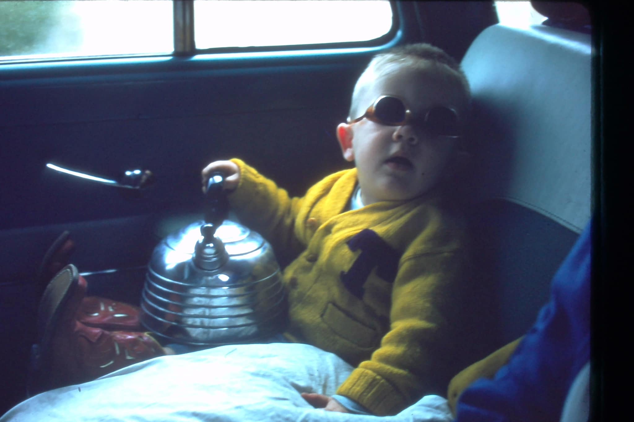 Leslie Jordan as a toddler sitting in a car and wearing a gold Tech sweater with a purple T