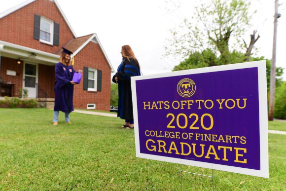 A photo of Dean Shank congratulating a May 2020 graduate in her front yard. There is a sign in the foreground of the photo that reads "Hats off to you 2020 college of Fine Arts Graduate"