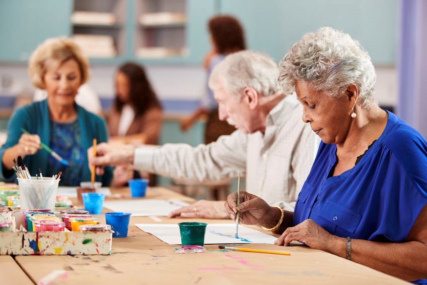 Three senior citizens are sitting at a table painting.
