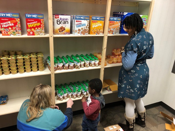 A woman and her child select items from the shelves of the auxiliary pantry with the help of a pantry worker.