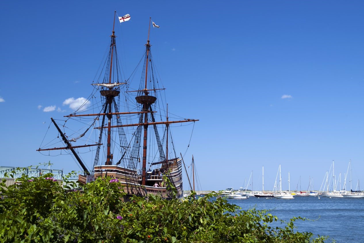 A photo of a ship with large masts in a harbor with sailboats behind it.