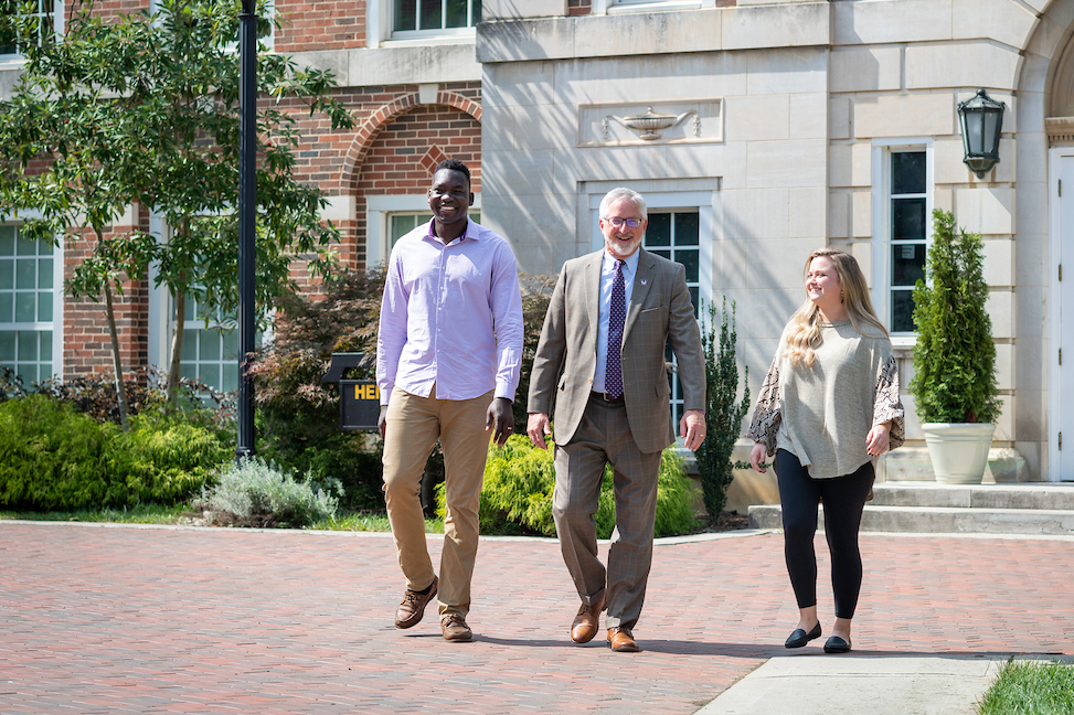 President Oldham walks in front of Henderson Hall with a couple of students