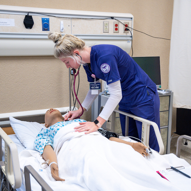 A nursing student checks the vitals of a sim patient.