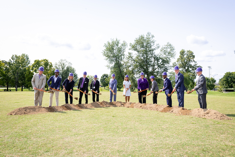 A group of people with purple hard hats break ground on the new engineering building.