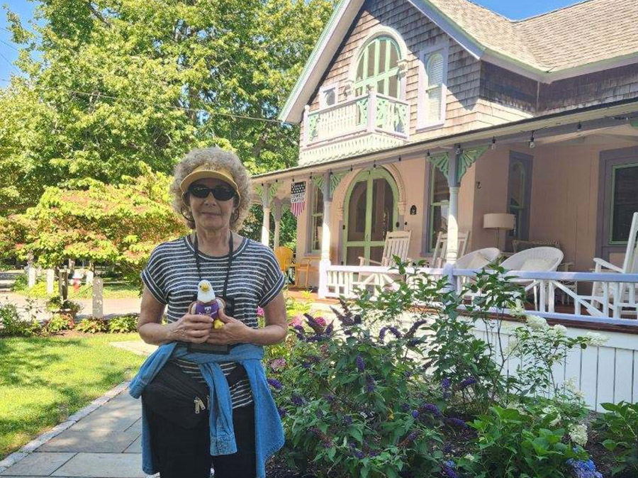 An woman standing in front of a pink house holding a plush animal of Awesome Eagle. 