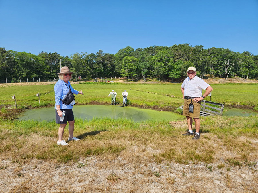 Two individuals standing in from of a pond. 