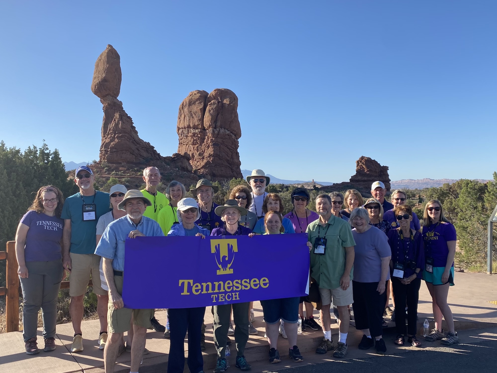 Tennessee Tech alumni stand in front of balancing rock at Arches National Park. They are holding a Tennessee Tech banner.