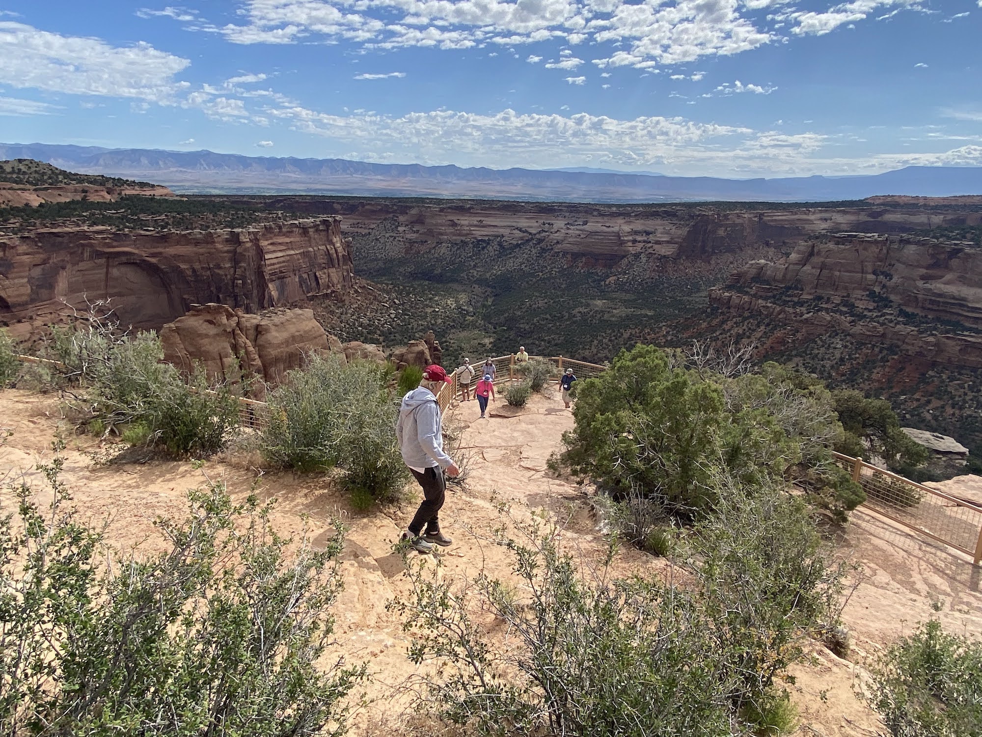 People walk to an overlook of a canyon cut in layered sandstone formations at Colorado National Monument