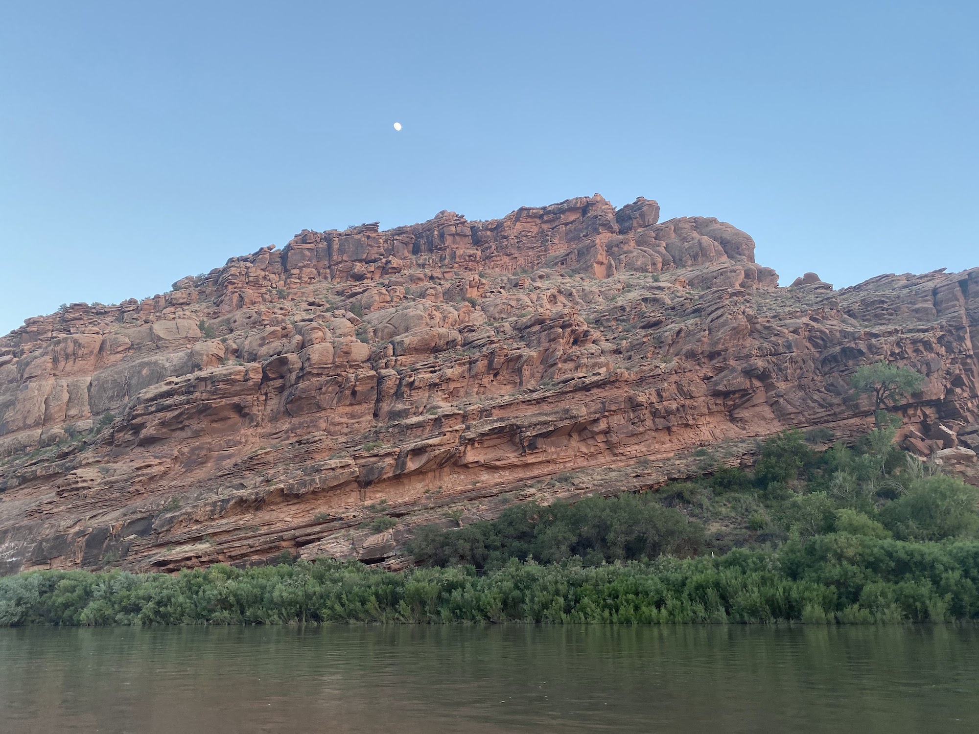 The moon over tilted layers of rock along the Colorado River